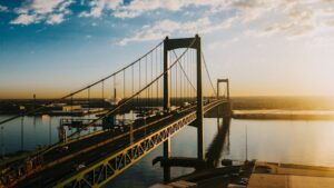 Breathtaking metal long bridge with cars over calm river under bright blue cloudy sky