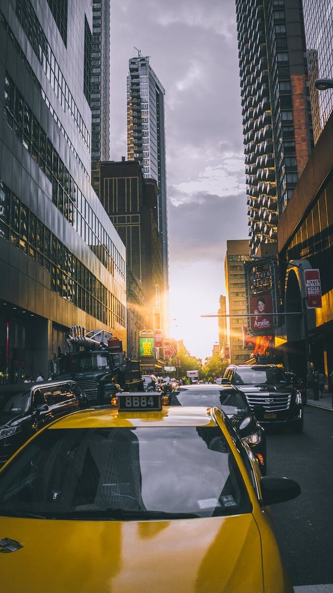 pexels-photo-876228-876228 Yellow taxi amidst busy New York City traffic with skyscrapers at sunset.